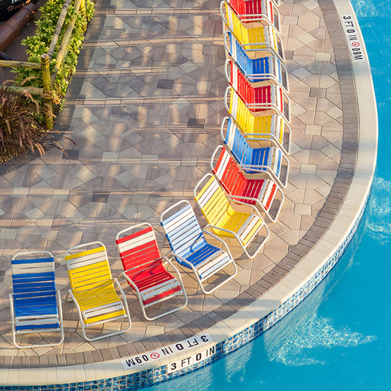Colorful low-profile vinyl strap sand chairs arranged along the edge of a commercial swimming pool.